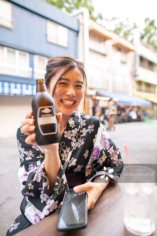 年轻女子身穿浴衣，在户外拿着啤酒杯图片素材