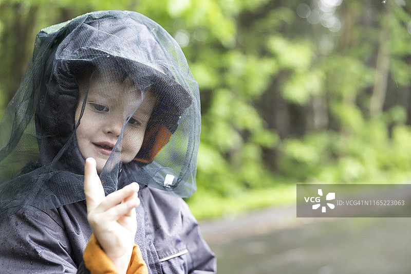 戴着蚊帐帽在露营地玩耍的红发小男孩图片素材