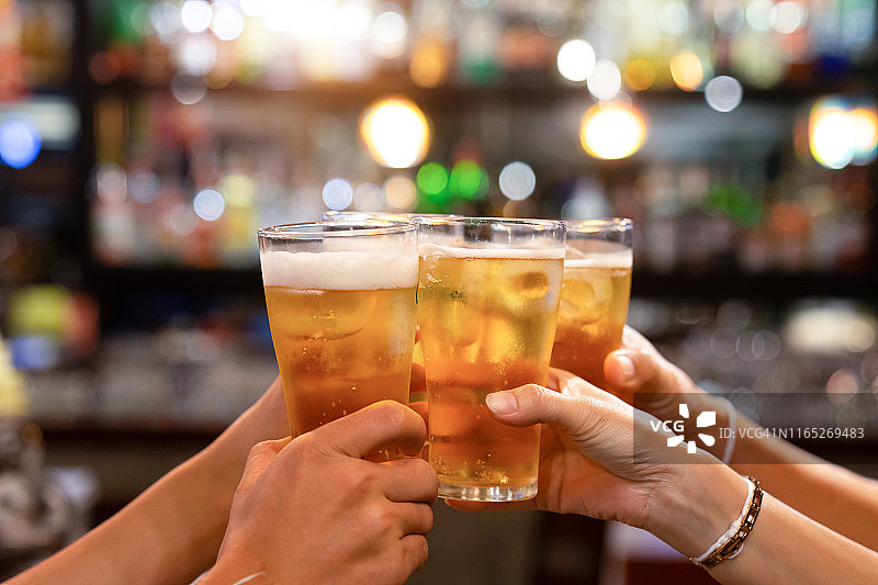 一群快乐的朋友在啤酒吧餐厅喝酒碰杯——年轻人在酷炫复古酒吧里一起玩乐的友谊概念——焦点集中在中部的品脱杯上——高ISO图像图片素材