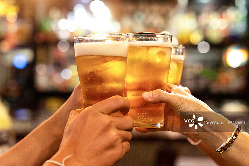 一群快乐的朋友在啤酒吧餐厅喝酒碰杯——年轻人在酷炫复古酒吧里一起玩乐的友谊概念——焦点集中在中部的品脱杯上——高ISO图像图片素材
