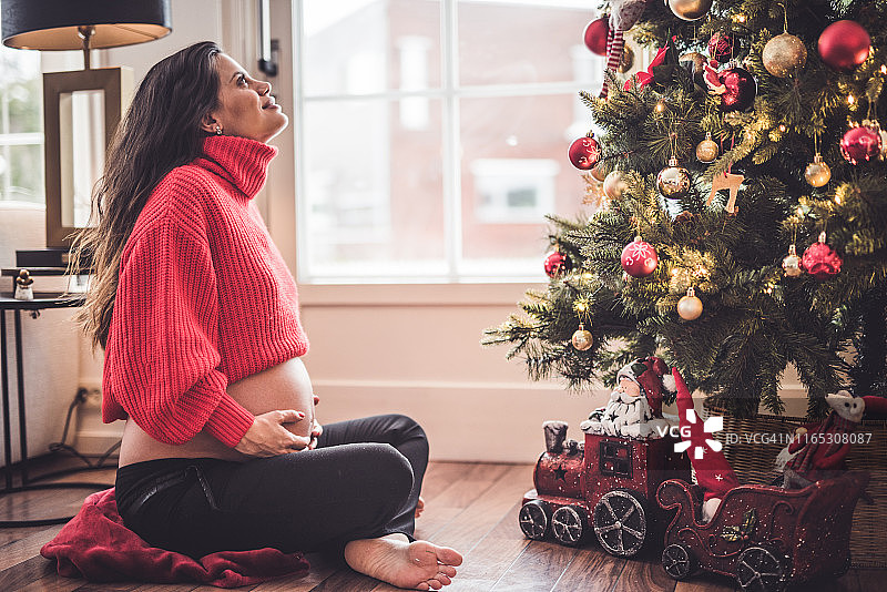 年轻漂亮的孕妇看着圣诞树图片素材