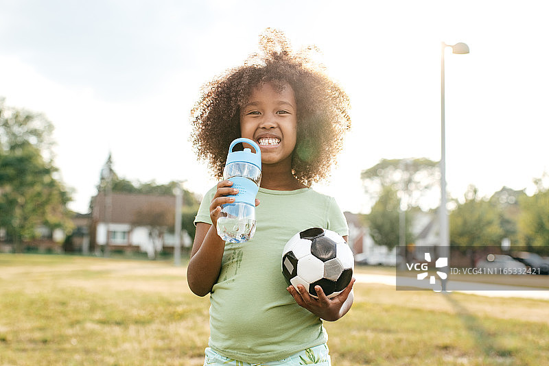 户外手持水瓶和足球的微笑女孩图片素材