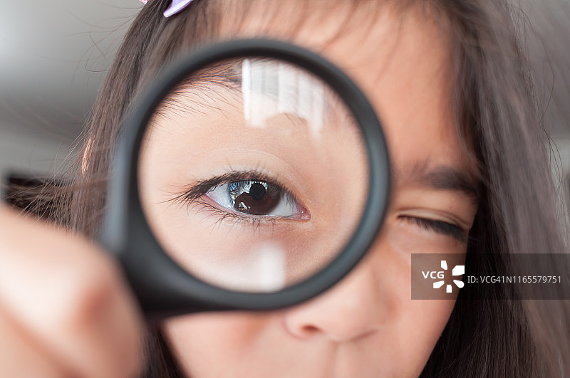 通过放大镜看着镜头的女孩图片素材