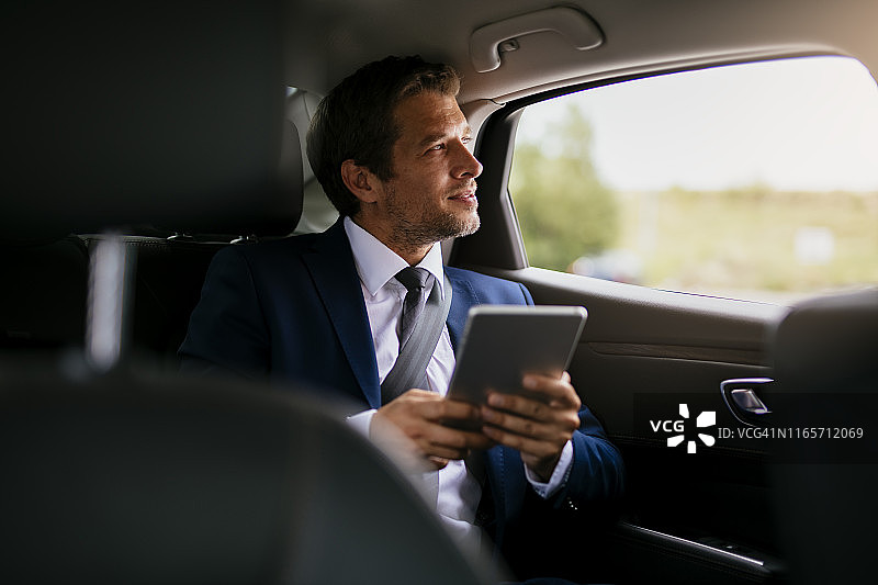 坐在汽车后座使用平板电脑的英俊商人图片素材