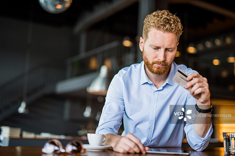 在咖啡店工作时进行在线投资的严肃年轻商人。图片素材