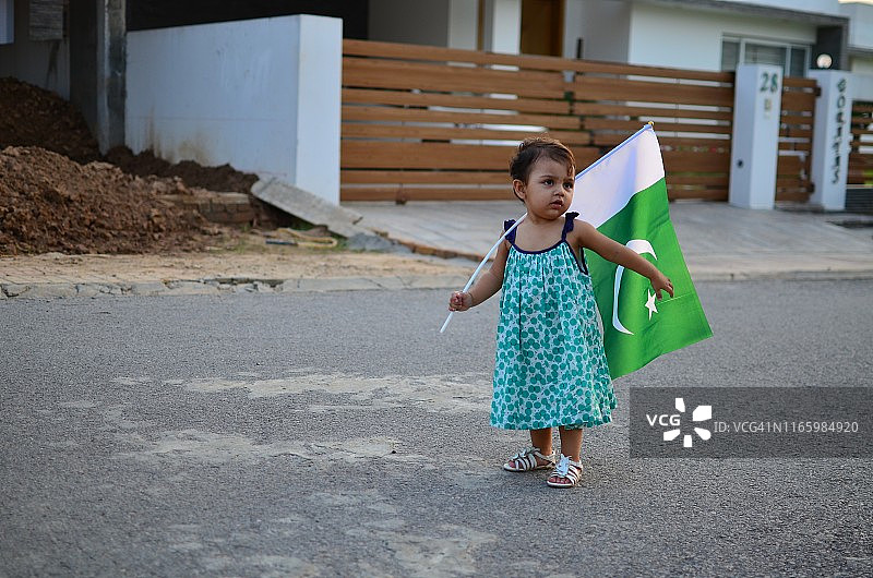 在巴基斯坦国庆日或独立日庆祝活动中，一个小女孩手持巴基斯坦国旗，身穿绿色连衣裙图片素材