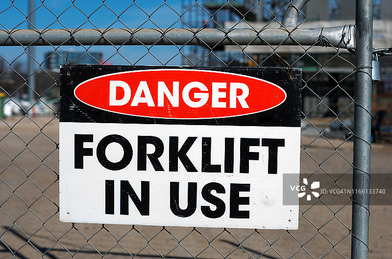建筑工地周围的金属网围栏上“危险：正在使用叉车”的警告标志图片素材