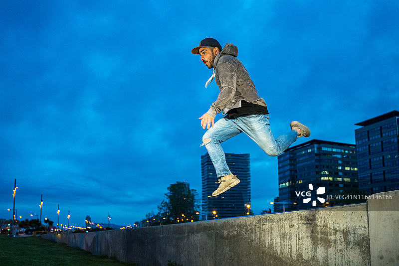 青年男子以跑酷风格跳跃，背景是巴塞罗那的天际线图片素材