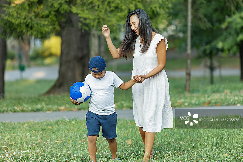 母亲和儿子在公园里踢足球图片素材