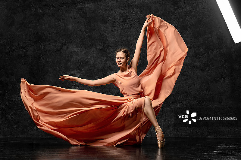 芭蕾舞女演员。一位年轻的芭蕾舞演员身穿桃色长裙和缎带足尖鞋，正在表演优雅的舞蹈动作。美丽的古典芭蕾，芭蕾舞工作室广告。图片素材