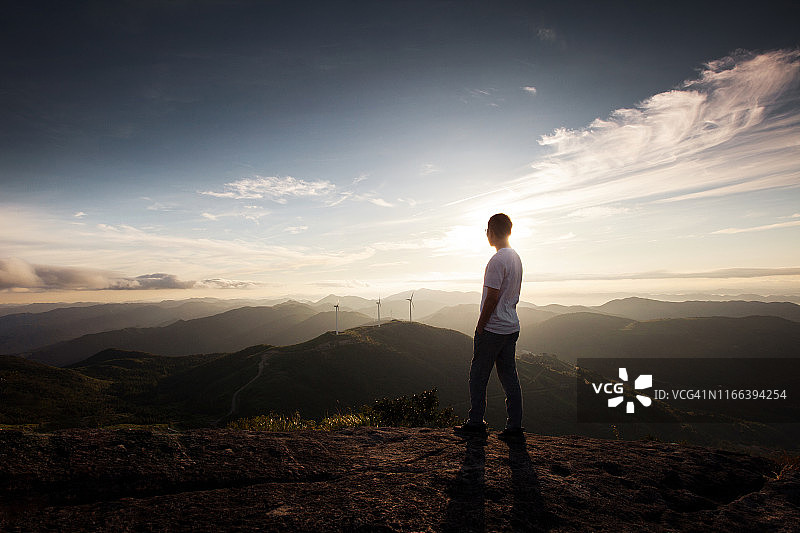 日出时站在夏日群山悬崖顶上的年轻男人图片素材