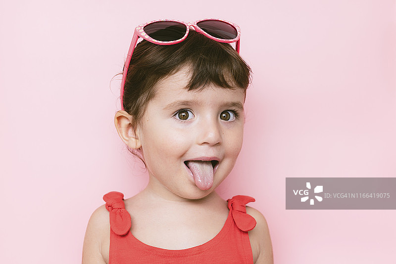 在粉色背景前吐舌头的小女孩肖像图片素材