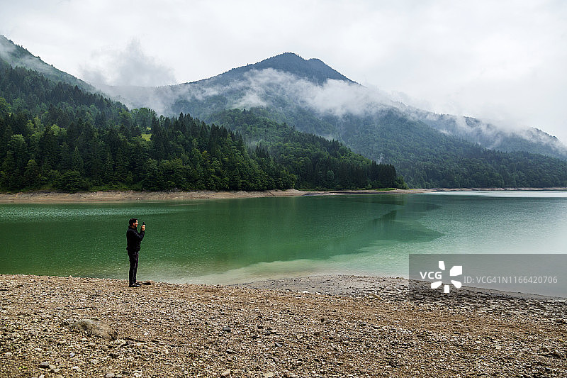 站在奥地利萨尔茨堡州维斯塔尔水库湖岸边用智能手机拍照的男人图片素材