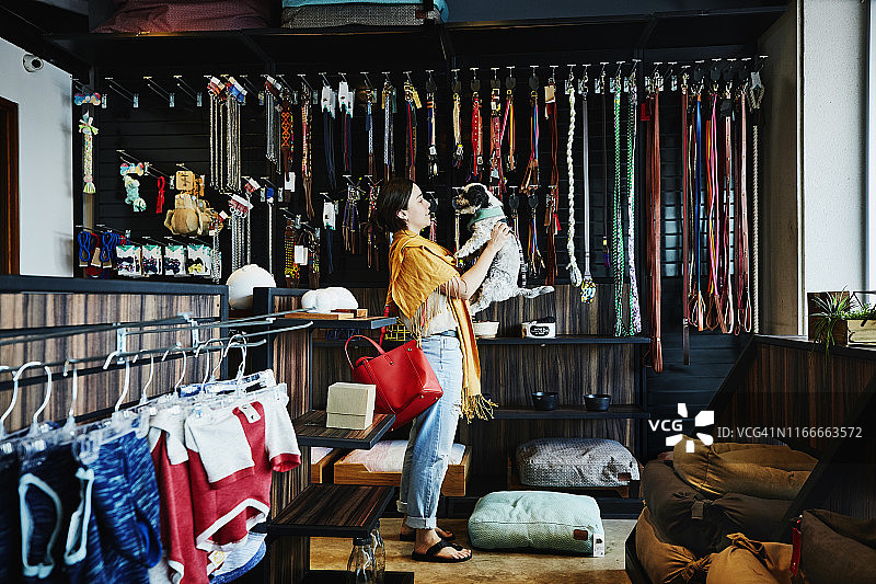 笑容满面的女人在宠物店购物，抱着小狗图片素材