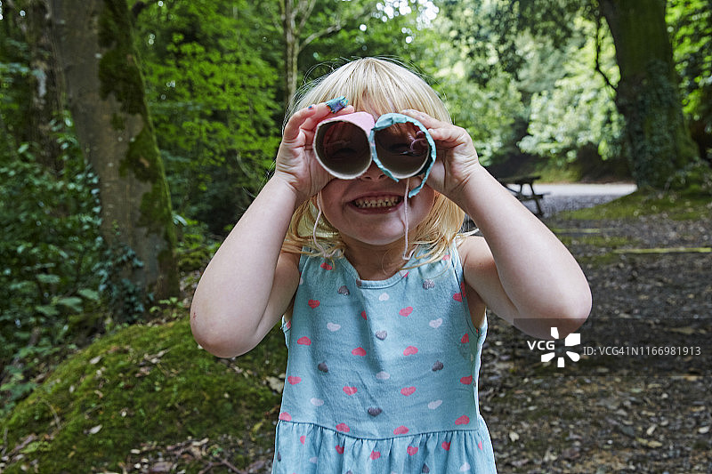 四岁女孩在森林里用自制玩具双筒望远镜观看图片素材