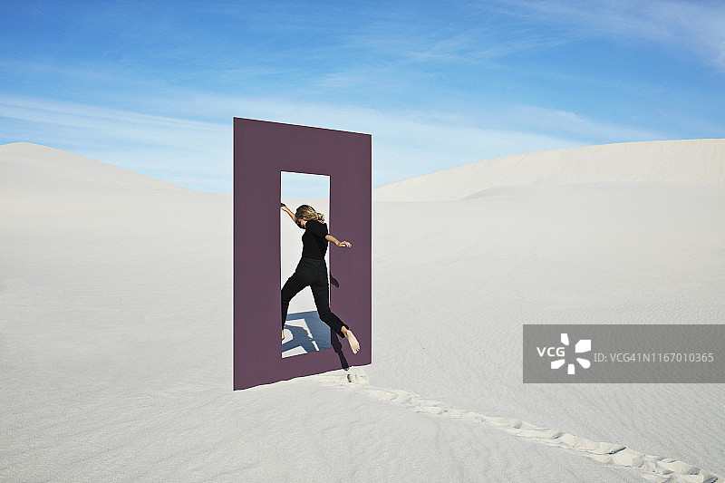 快乐的年轻女子在沙漠中跳过门框图片素材