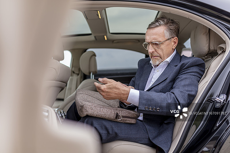 在汽车后座使用手机的工作过度的商人图片素材
