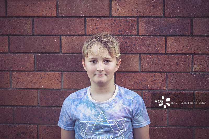 站在砖墙前微笑的少年图片素材