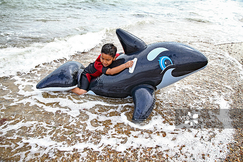 穿潜水服的男孩在沙滩上玩充气海豚图片素材