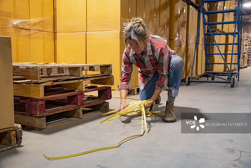 工业仓库工作场所安全主题：一名妇女清理仓库中的绊倒隐患图片素材