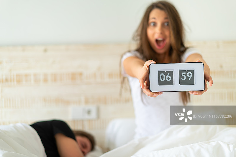 太晚了，女人在床上被闹钟吵醒图片素材