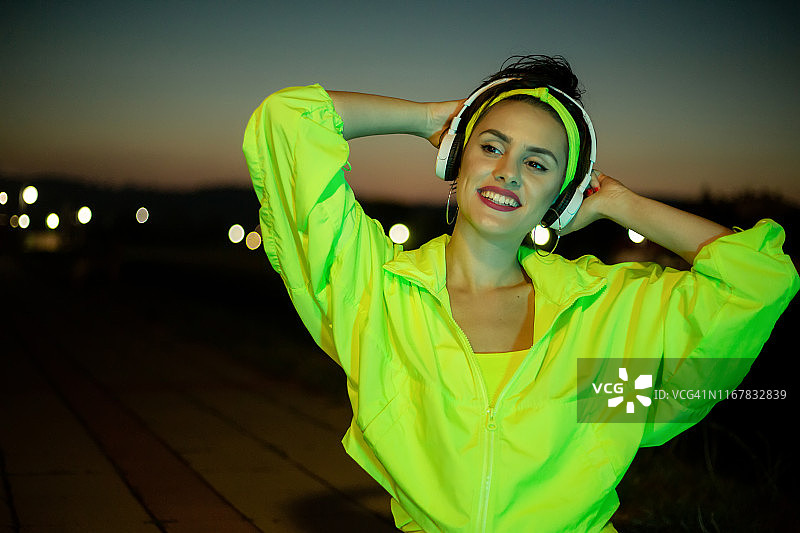 在长廊上戴着霓虹外套听音乐的可爱小女孩图片素材