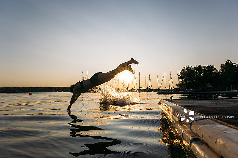 夏日：夕阳下，年轻女子从码头跳入湖中图片素材