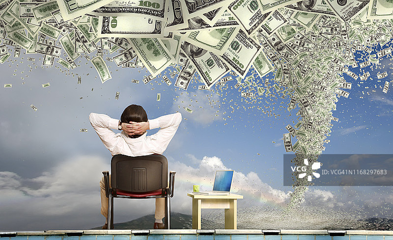 拿着笔记本电脑看着金钱风暴的商人图片素材