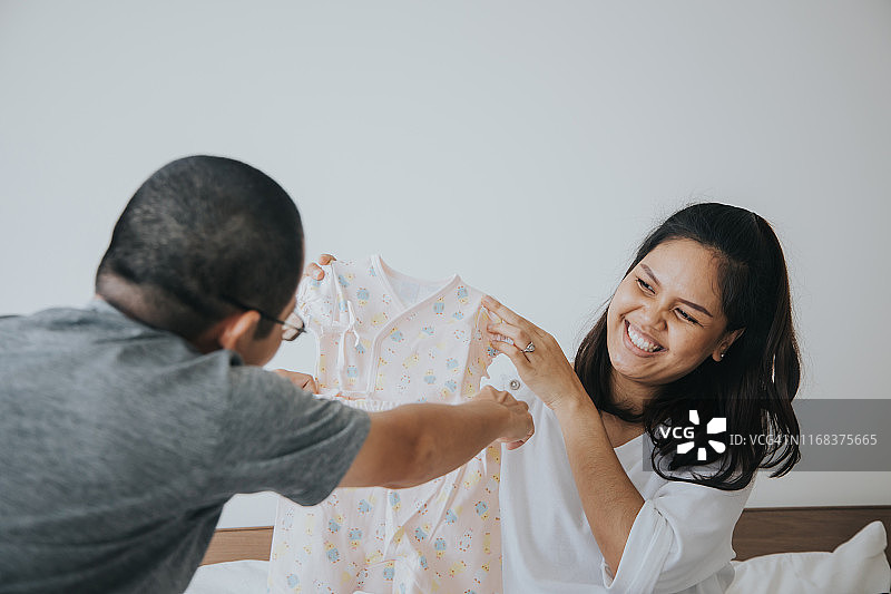 泰国孕妇夫妇在家选择婴儿服装，迎接新家庭成员图片素材