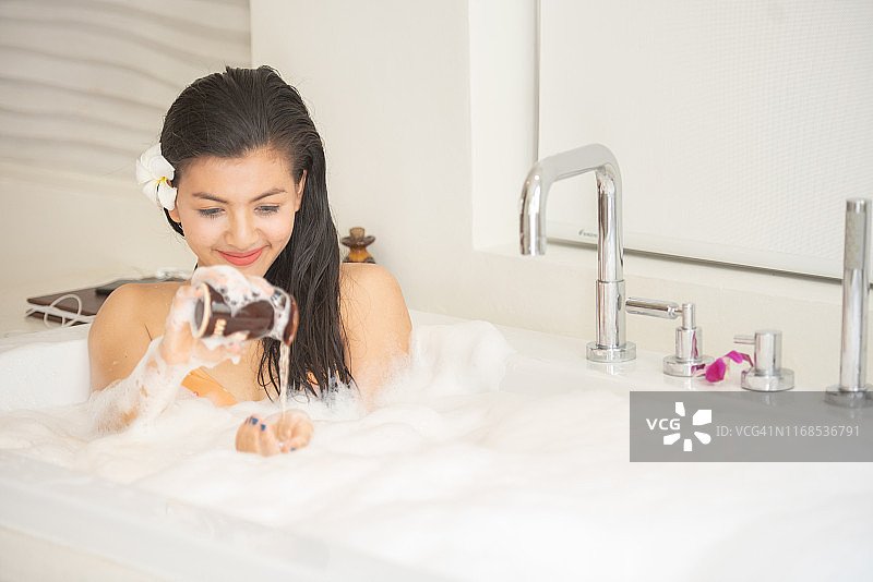 在白色浴缸中的亚洲女孩，浴缸里有洗发水和香皂图片素材