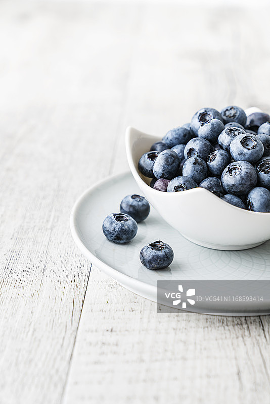 明亮木质背景上白色瓷盘里的蓝莓图片素材