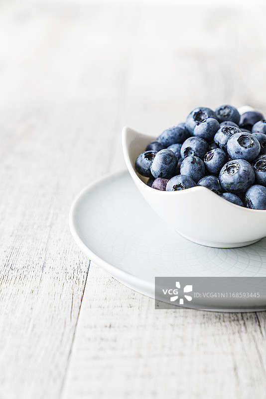 明亮木质背景上白色瓷盘里的蓝莓图片素材