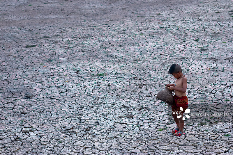 站在干旱地区龟裂土地上的亚洲儿童图片素材