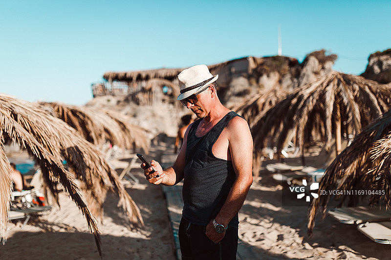 在阳光明媚的海滩上使用智能手机的中年男人图片素材