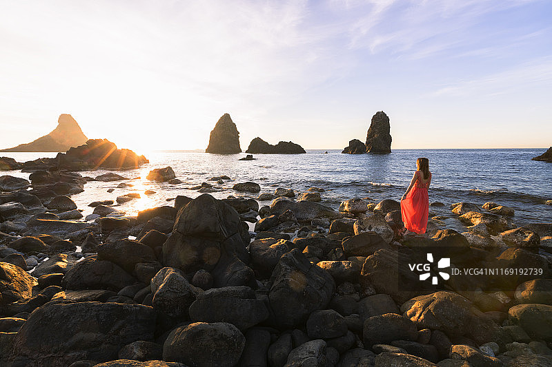 日出时分，女人在意大利西西里卡塔尼亚省阿奇特雷扎欣赏独眼巨人岩图片素材