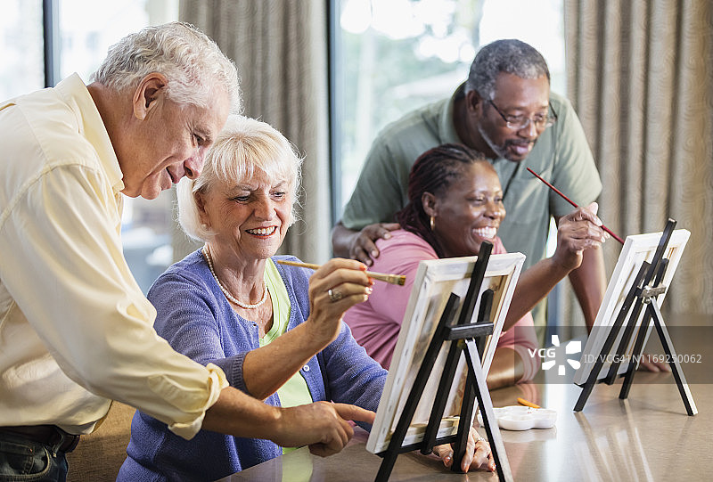 年长的女人和朋友在画布上绘画，配偶在一旁观看图片素材