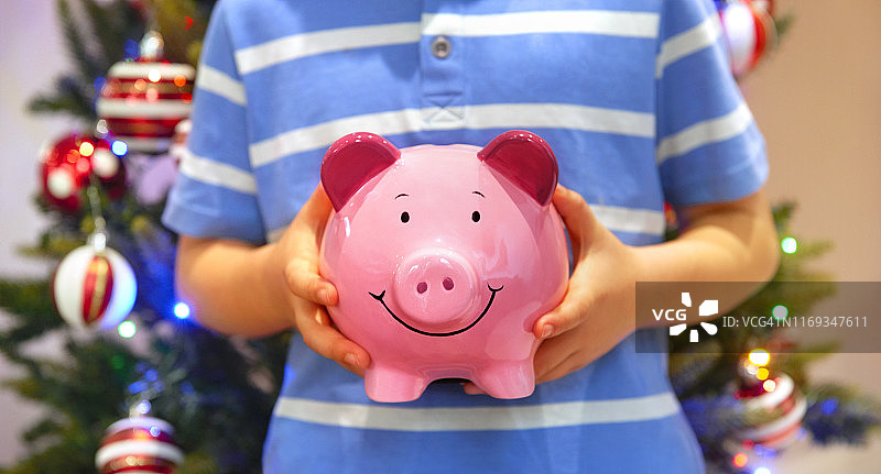 儿童在圣诞树前拿着小猪存钱罐图片素材
