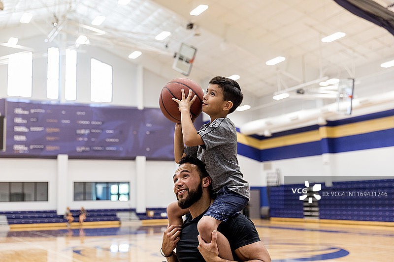 父亲让儿子坐在肩膀上在健身房投篮图片素材