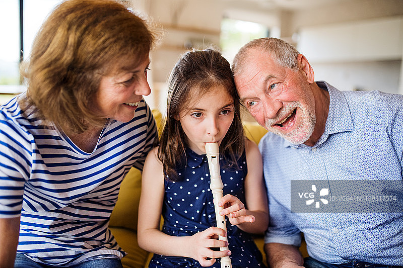 小女孩和祖父母坐在室内沙发上玩竖笛图片素材
