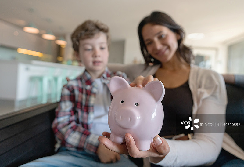 漂亮的母亲和儿子在沙发上放松，前景是一个粉红色的储蓄罐图片素材