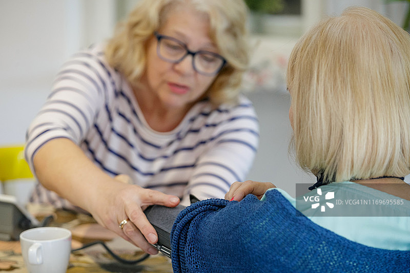 年长的妇女在朋友的手臂上放置臂带来测量血压图片素材