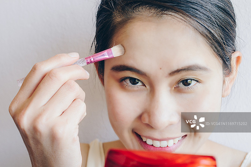 亚洲女性用刷子在脸上涂抹遮瑕膏图片素材