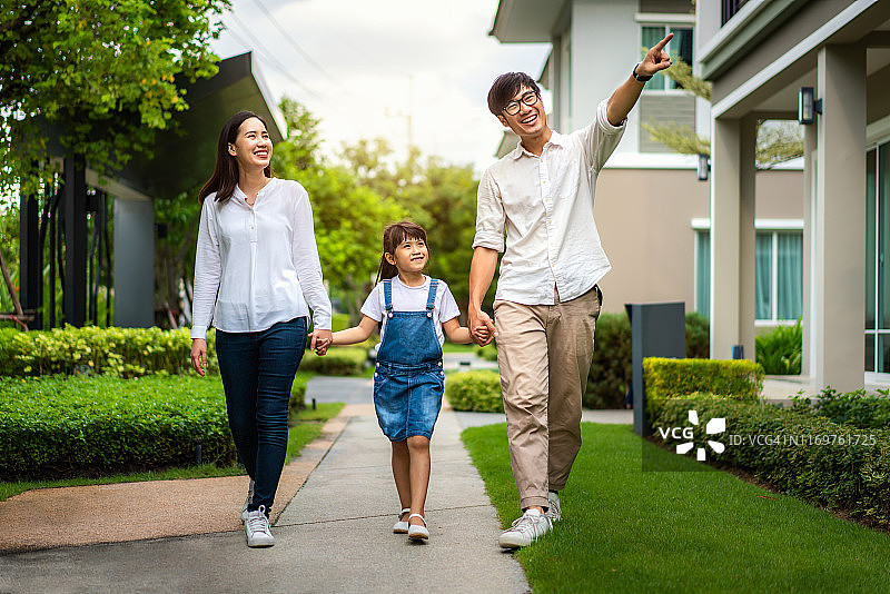 亚洲家庭在村庄新房前合影：女儿指向新家，满脸幸福图片素材