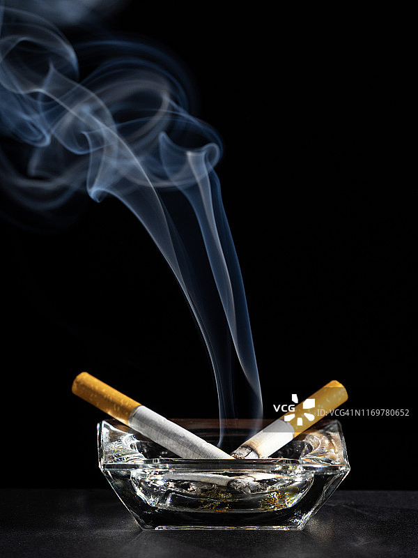 黑色背景上烟灰缸里的点燃的香烟和烟雾图片素材