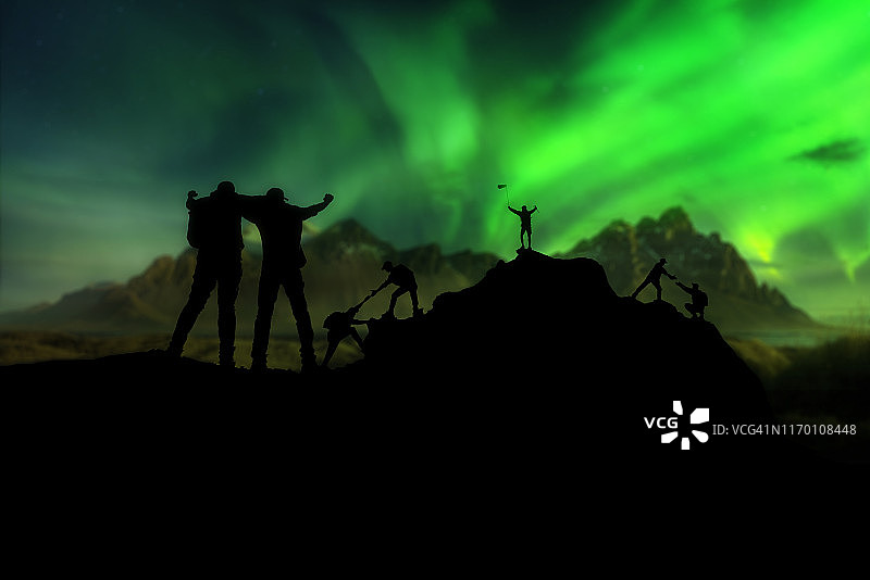 站在山上的攀登团队和北极光背景。团队合作、互助、成功、获胜者和领导力概念图片素材