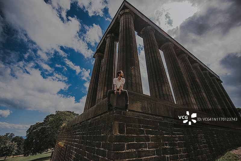 男人坐在苏格兰爱丁堡卡尔顿山的国家纪念碑旁图片素材