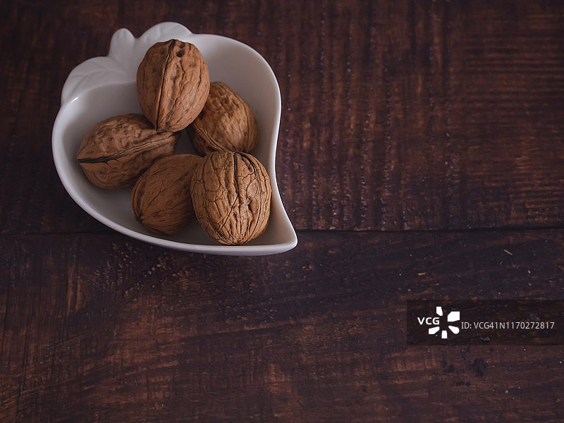 秋季水果：旧木桌子上心形瓷碗中的一组坚果图片素材