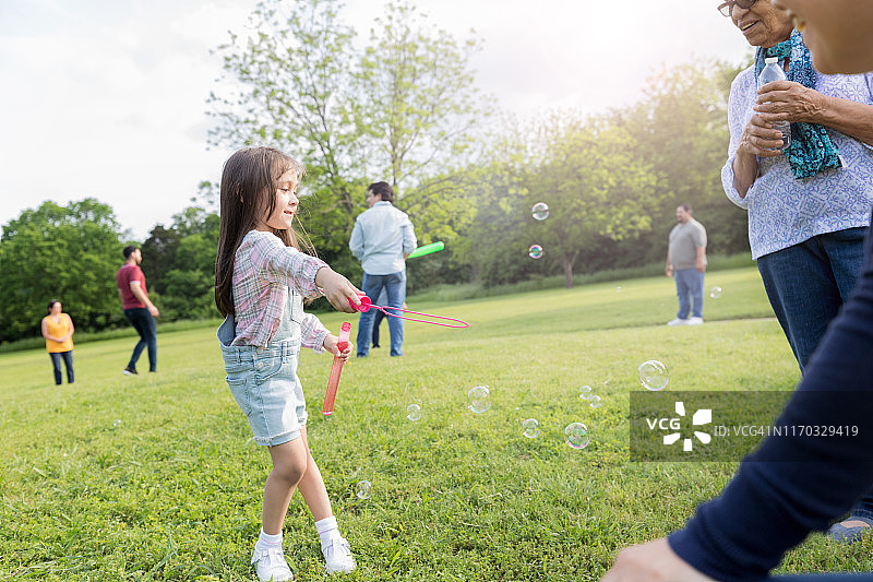 母亲和祖母看着小女孩用魔杖吹泡泡图片素材