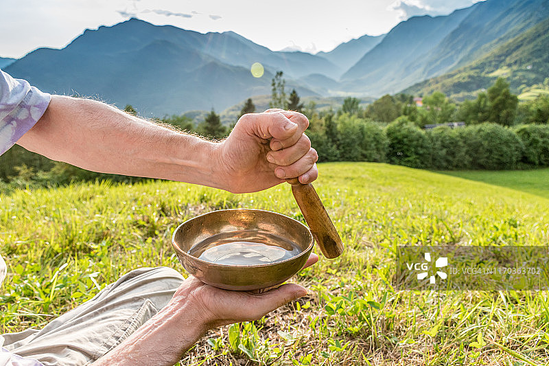 日落时分，男子在山边演奏西藏手工颂钵特写图片素材