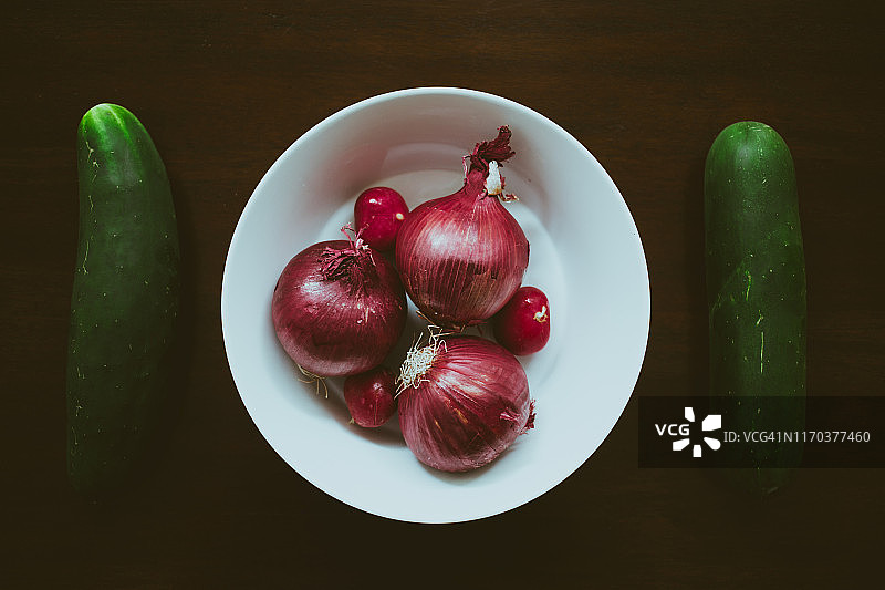 一碗未剥皮的红洋葱和萝卜，两侧是两根黄瓜图片素材